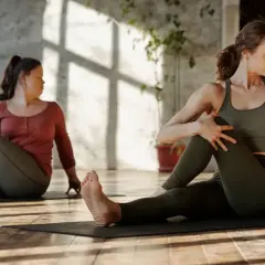 Dwie kobiety wykonują skręt tułowia na macie. To ćwiczenie, znane jako stretching, poprawia elastyczność.