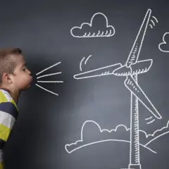 Chłopiec dmucha, wprawiając w ruch wiatrak narysowany kredą. To świetne ćwiczenia oddechowe dla dzieci, które uczą się o energii wiatrowej.
