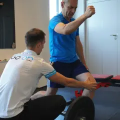 Fizjoterapeuta pomaga mężczyźnie w prawidłowym wykonaniu ćwiczenia podczas treningu oporowego.