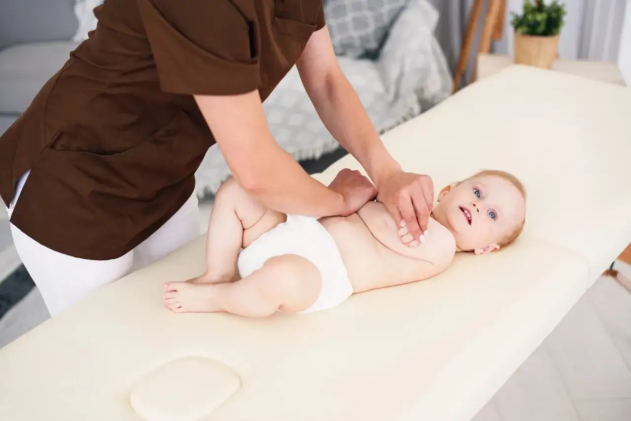 Niemowlę na masażu. Terapeuta wykonuje ćwiczenia metodą Vojty, delikatnie uciskając rączki dziecka.