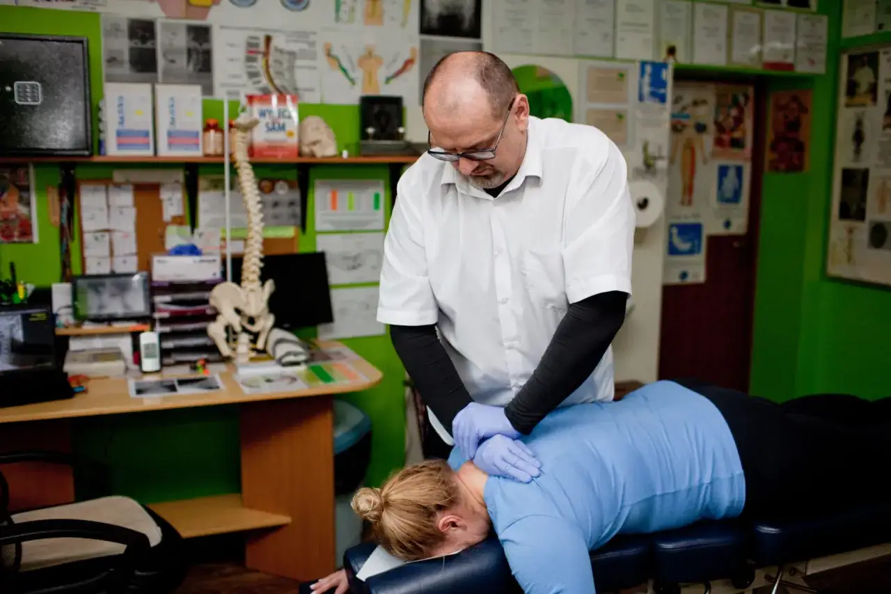 Chiropraktyka co to? Terapeuta w rękawiczkach delikatnie uciska szyję pacjentki leżącej na kozetce.