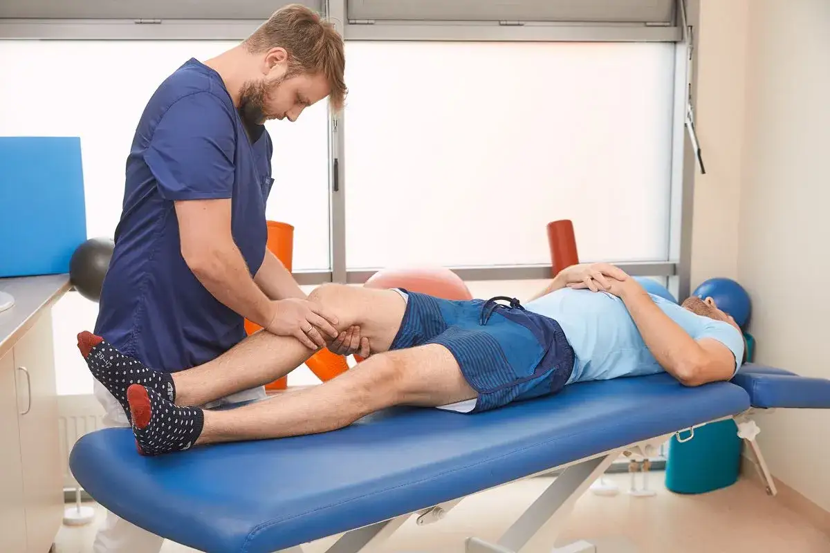 Fizjoterapeuta pracuje z pacjentem po endoprotezie kolana. Ważne, czego nie wolno robić po endoprotezie kolana, by uniknąć powikłań.