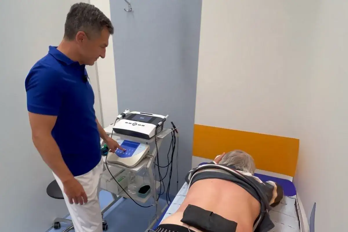 Fizjoterapeuta ustawia parametry na aparacie do elektrostymulacji. Pacjent leży na łóżku, czeka na zabieg EMS.