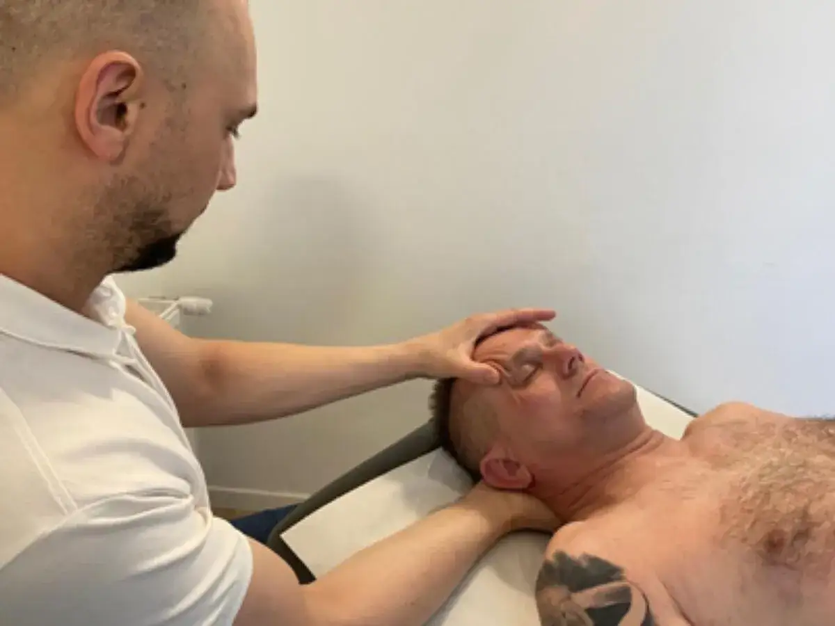 Fizjoterapeuta delikatnie masuje kark pacjenta, łagodząc napięcie i ból po przewianiu szyi.