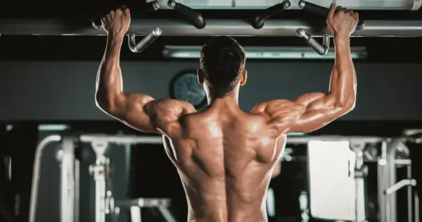 Mężczyzna wykonuje podciąganie na drążku, napinając potężne **biceps**y.